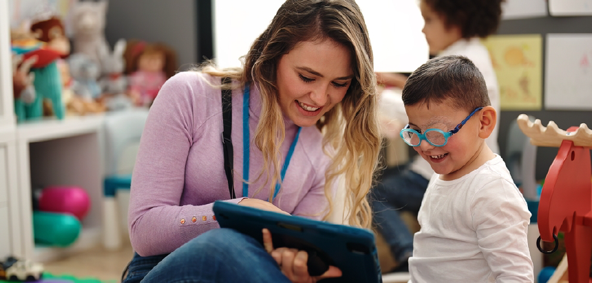 Female teacher showing assistive technology device to young boy wearing eye patch