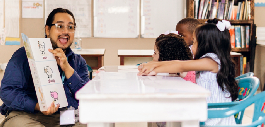 Male teacher reading picture book to young children across a table